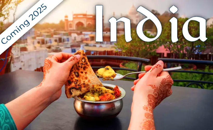 A woman with henna-adorned hands enjoying a vegan Indian dish with the Taj Mahal in the background, highlighting India's cultural and culinary experiences